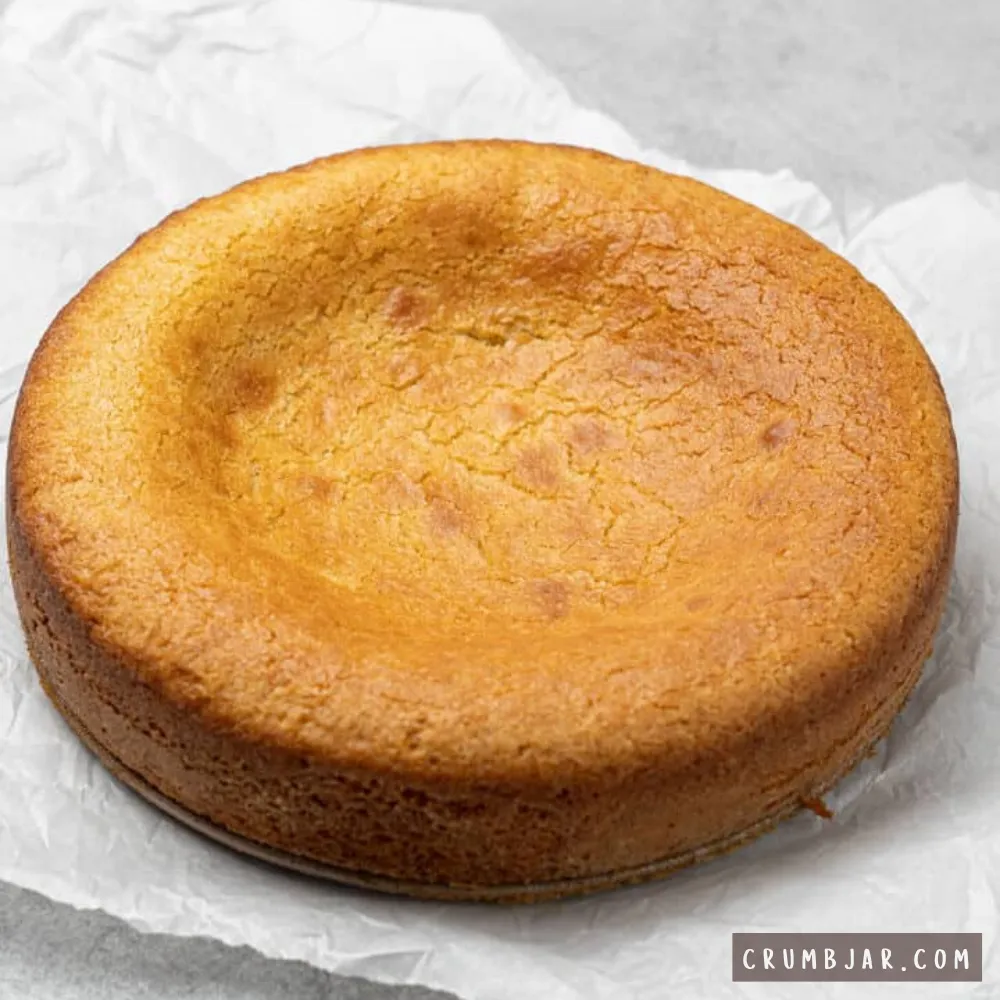 A round golden-brown baked cake resting on white parchment paper with a noticeably sunken center, illustrating "My cake sank in the middle."