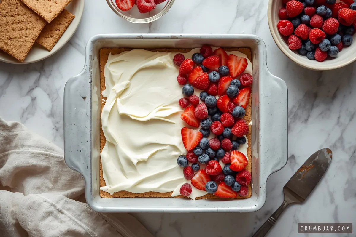 Overhead view of layering fresh mixed berries over whipped cream and graham crackers in a baking dish for no-bake berry icebox cake.