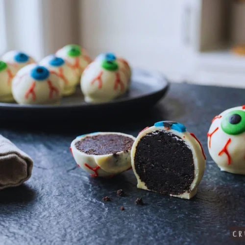 Halloween eyeball Oreo truffles displayed on a dark countertop with a sliced truffle revealing the fudgy cookie center.