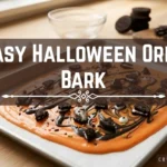 Orange and black chocolate bark topped with crushed Oreo cookies, candy eyes, and sprinkles on a baking sheet, with text overlay reading "Easy Halloween Oreo Bark".